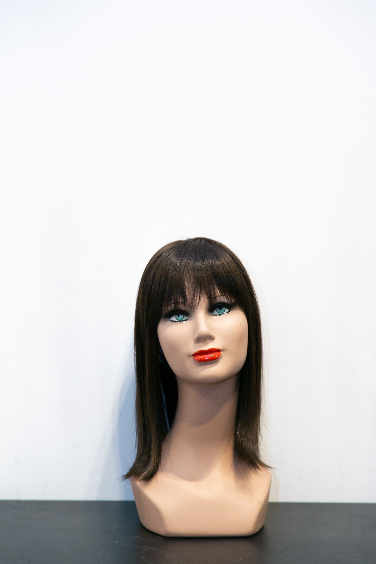 Testa di manichino con parrucca marrone, frangia e rossetto rosso.