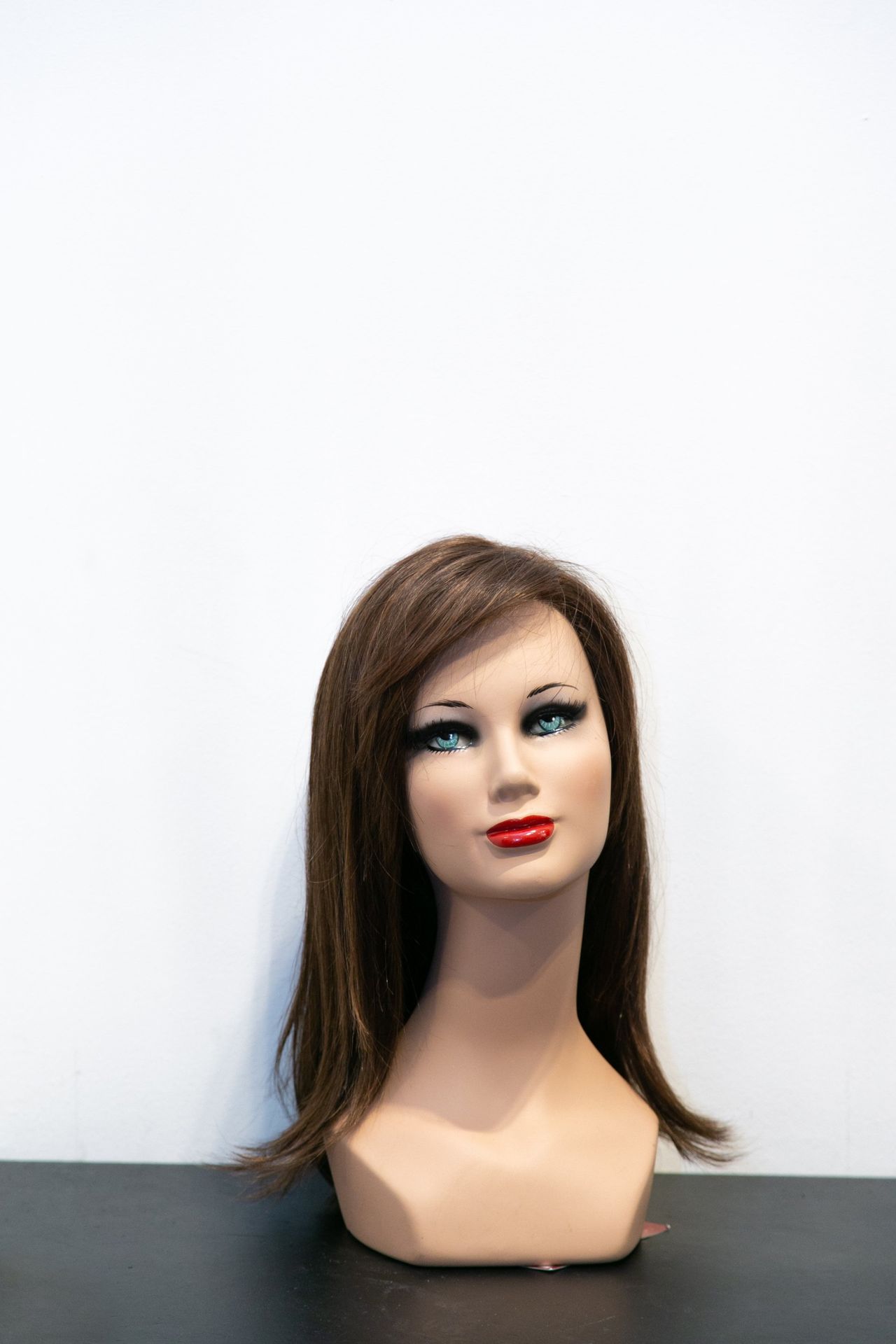 Testa di manichino con capelli castani e rossetto rosso su sfondo bianco.