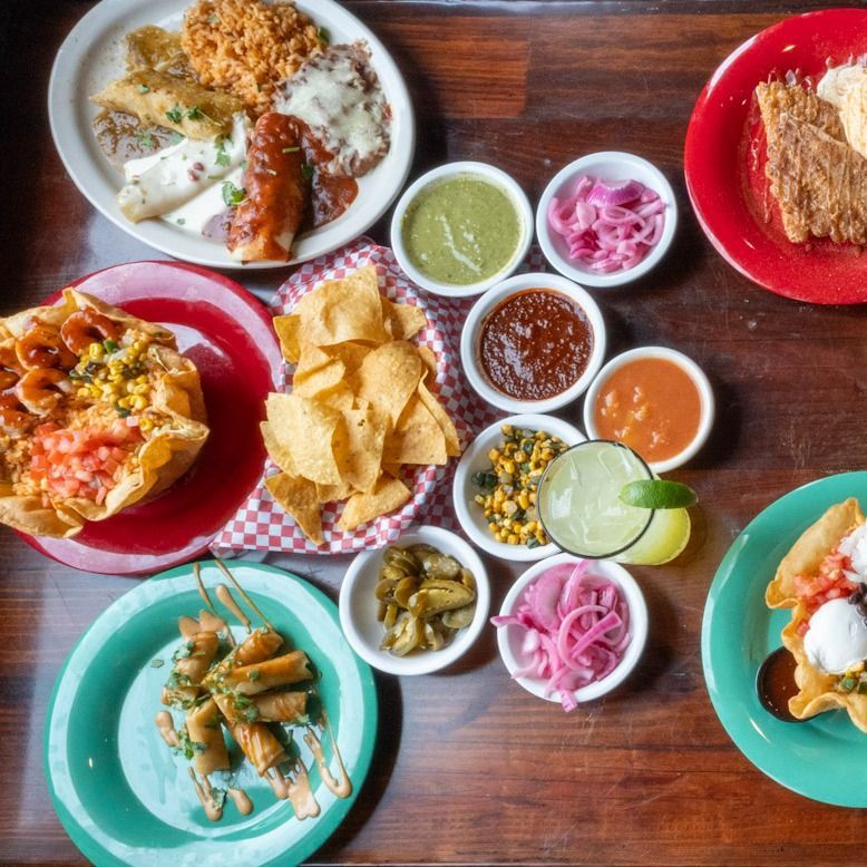 Overhead shot of a table laden with Mexican food, including tacos, chips with various salsas, and margaritas.