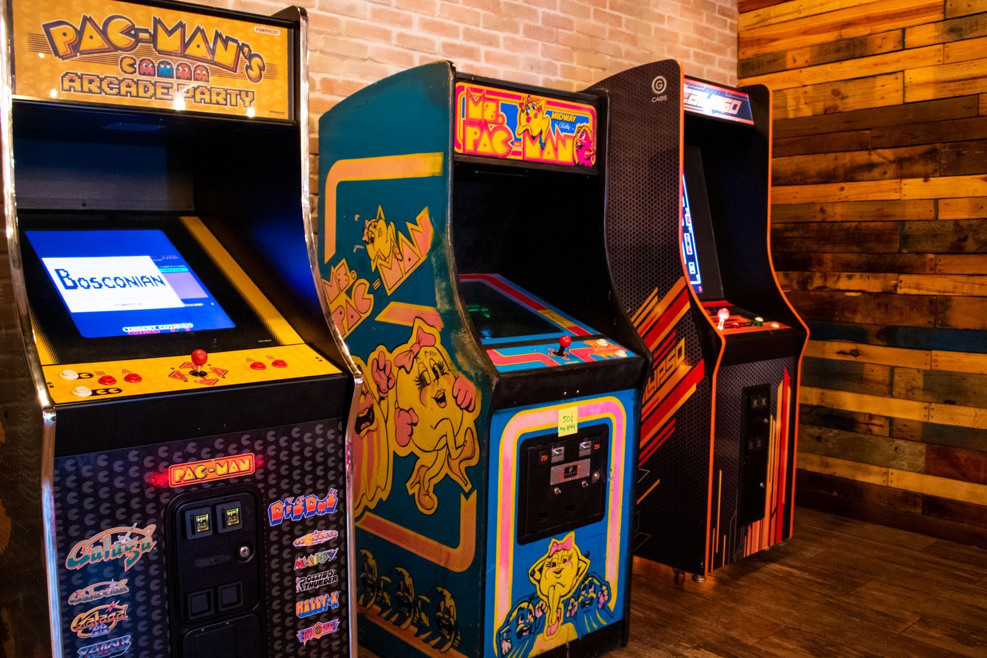 Three arcade machines are lined up next to each other in a room.