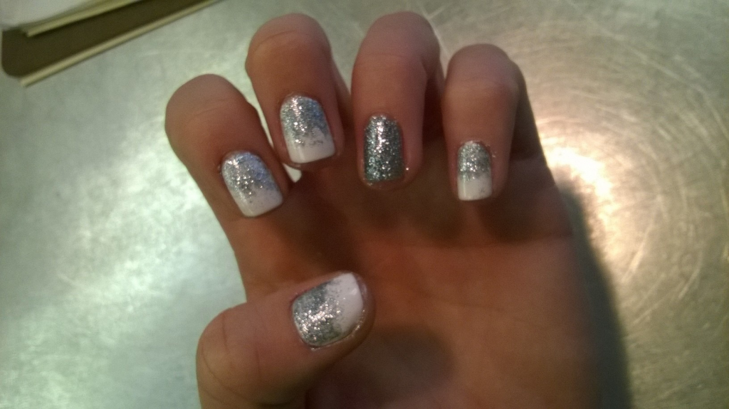 Hand with silver glitter nail polish curled into a loose fist on a metallic surface.