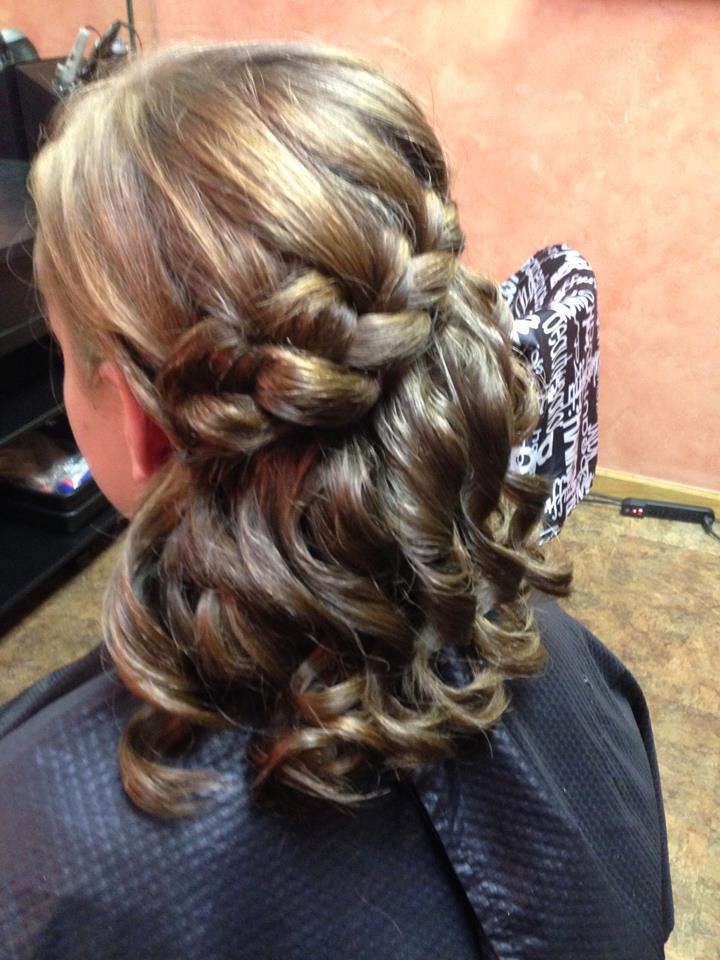Intricate braided updo with loose curls in blonde and brown hair, shown from the back at a salon.