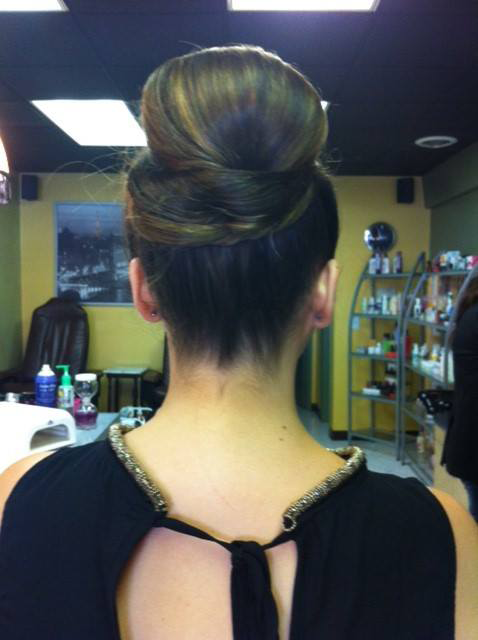 Back view of a woman with an elegant updo hairstyle in a salon, showing a tied black top with gold straps