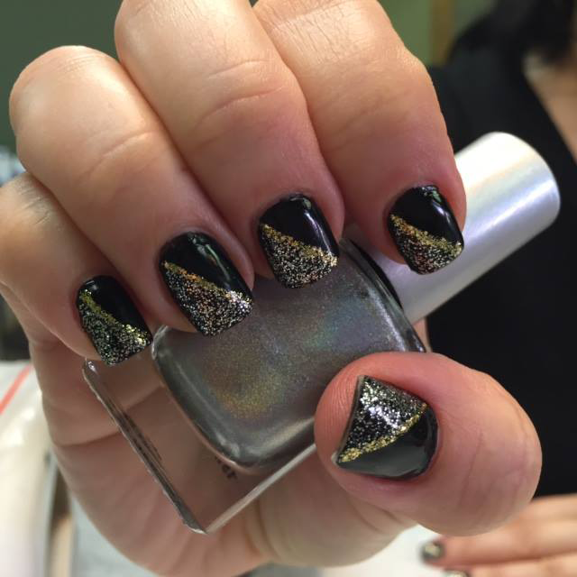 Close-up of hand with black and gold glitter manicure holding a silver nail polish bottle