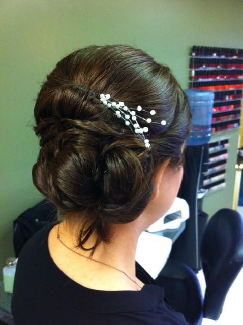 Woman with dark hair in an elegant bun, decorated with white pins, viewed from behind in a salon.