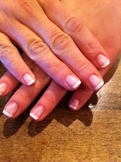 Close-up of manicured hands with French tips resting on a wooden table