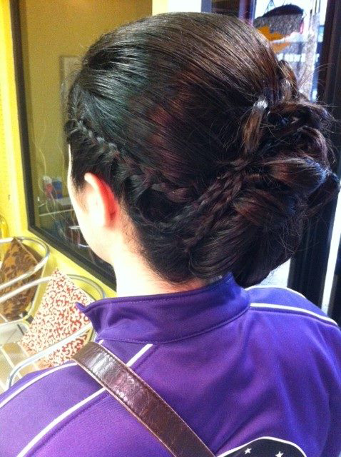 Person with dark hair in a bun wearing a purple jacket, viewed from behind in a mirror.