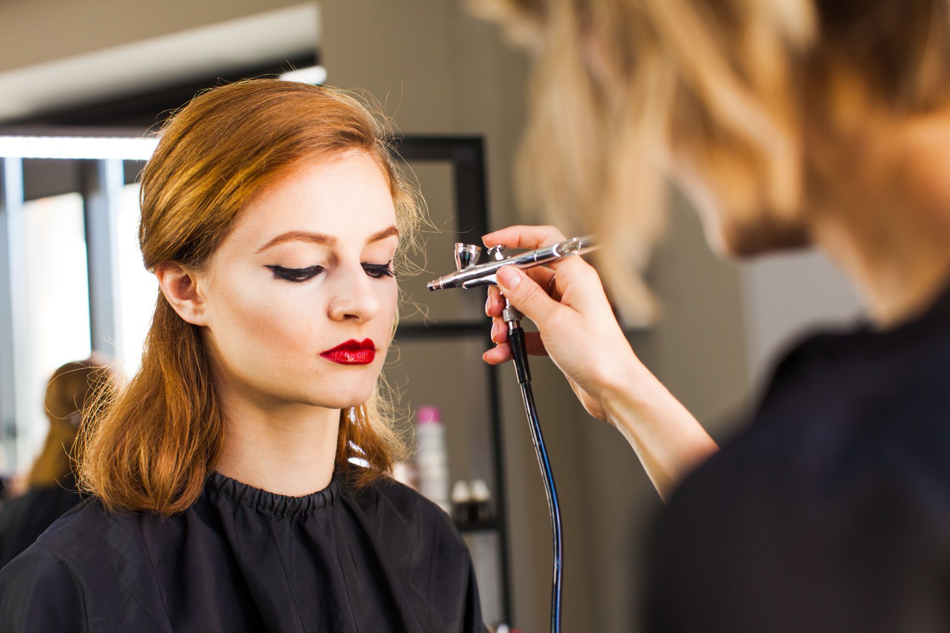 Makeup artist applying eyeliner to a seated woman in a salon