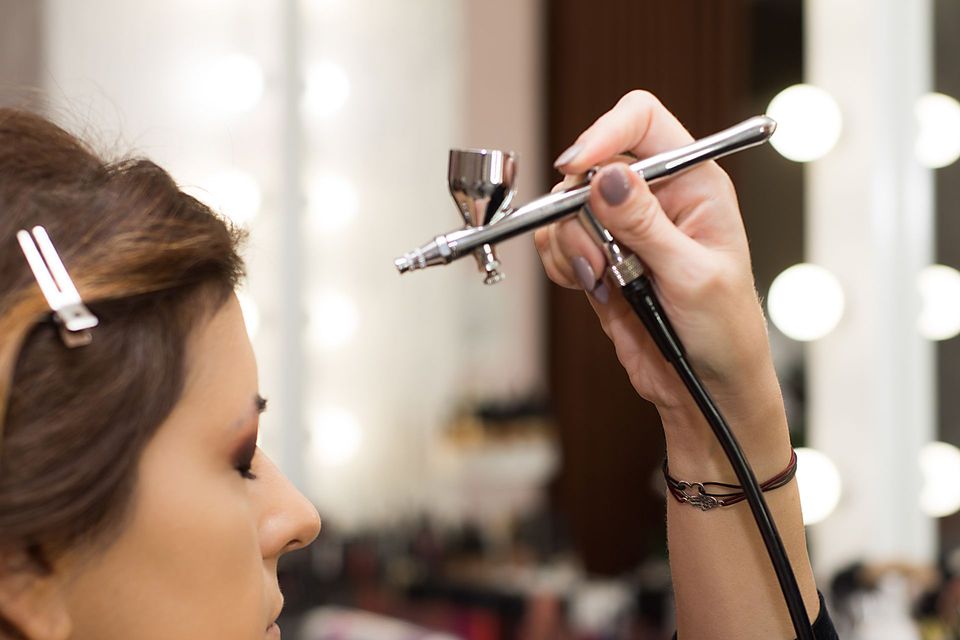 Makeup artist airbrushing foundation on a client in a salon