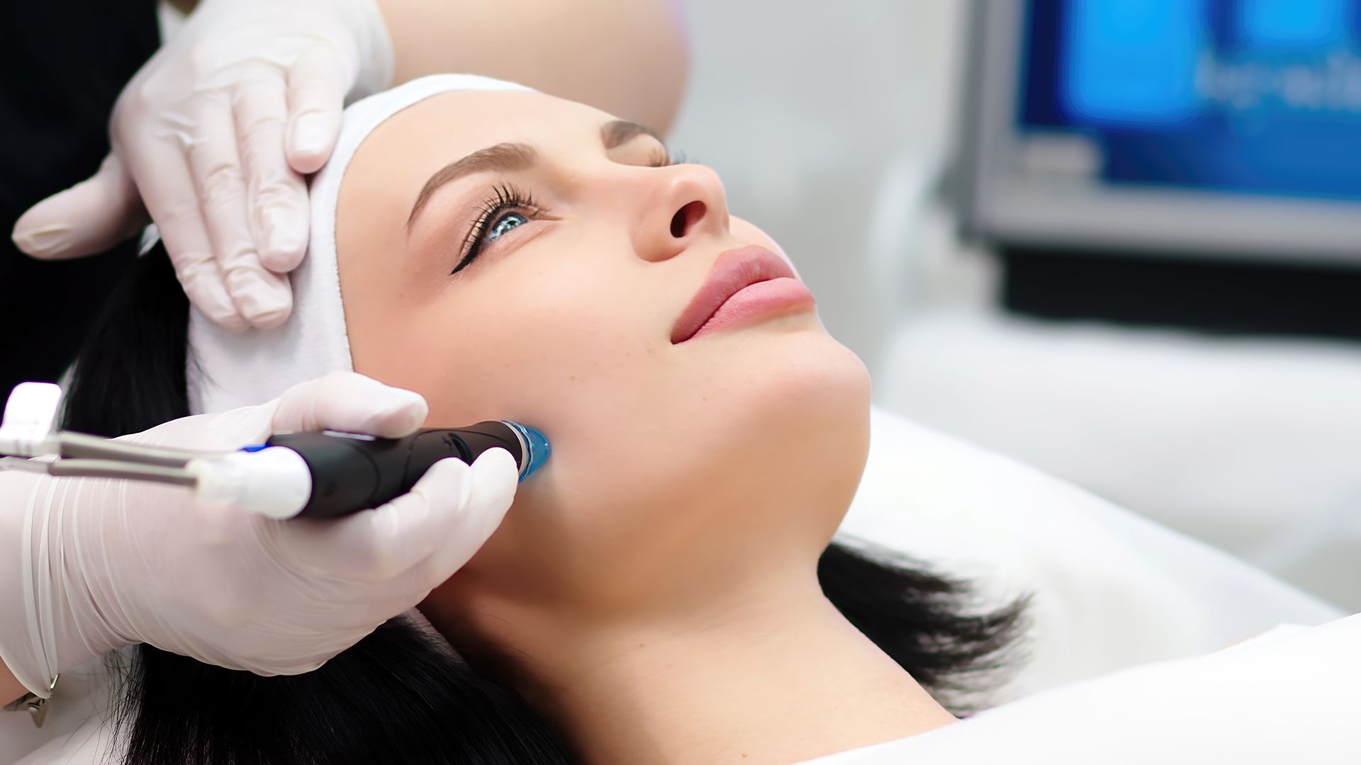 Cosmetic treatment on a woman’s face with gloved hands using a handheld device in a clinic