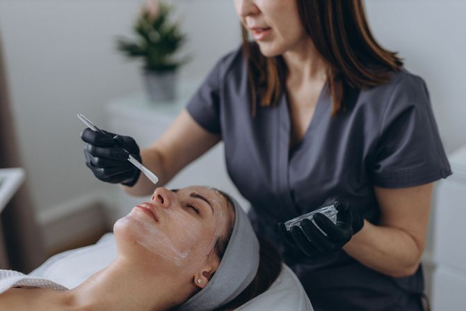 Cosmetologist applying a facial treatment to a woman lying on a spa bed