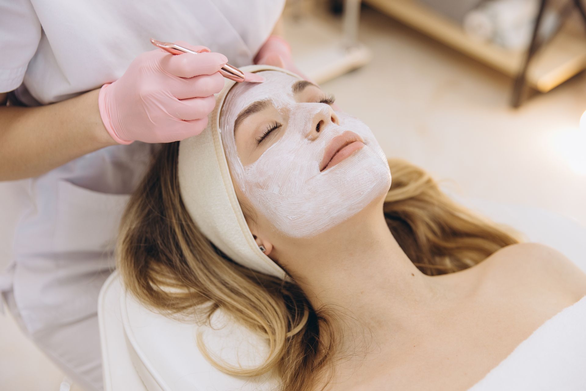 Spa treatment with a woman wearing a white face mask as another hand applies product to her forehead