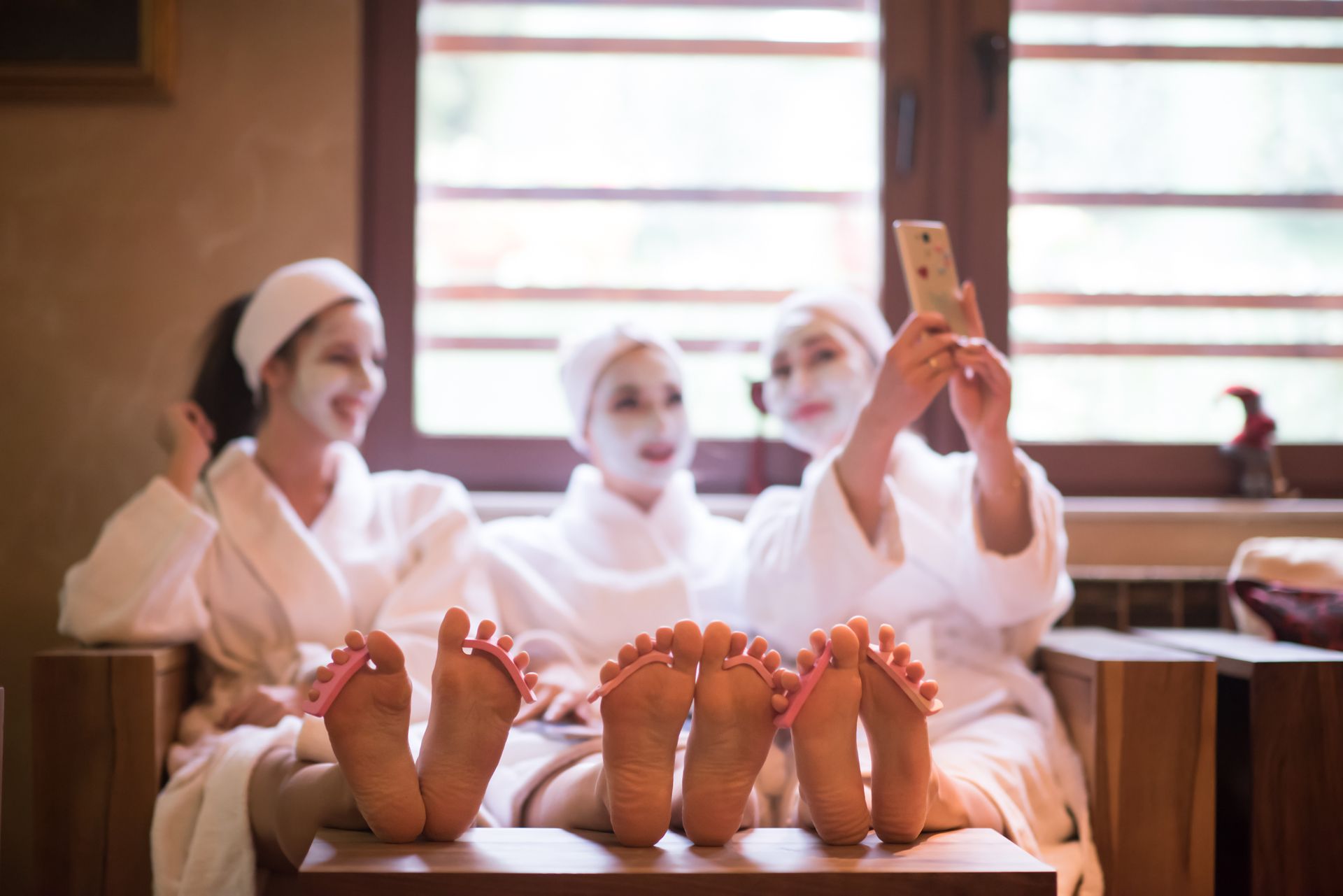 Three people in white robes and towels relax in a spa, one taking a selfie with bare feet in the foreground