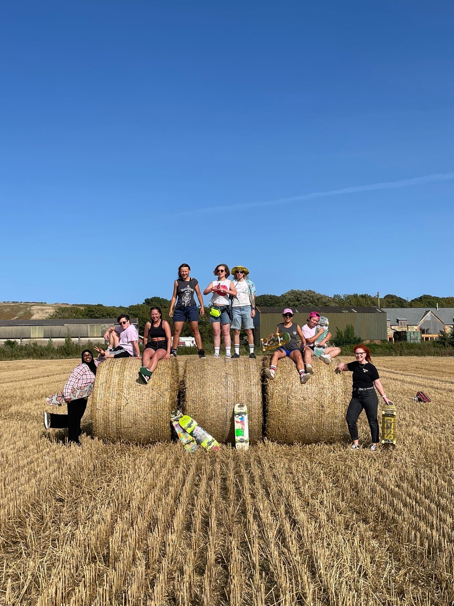 Group posing on hay bales in a harvested field under a clear blue sky.