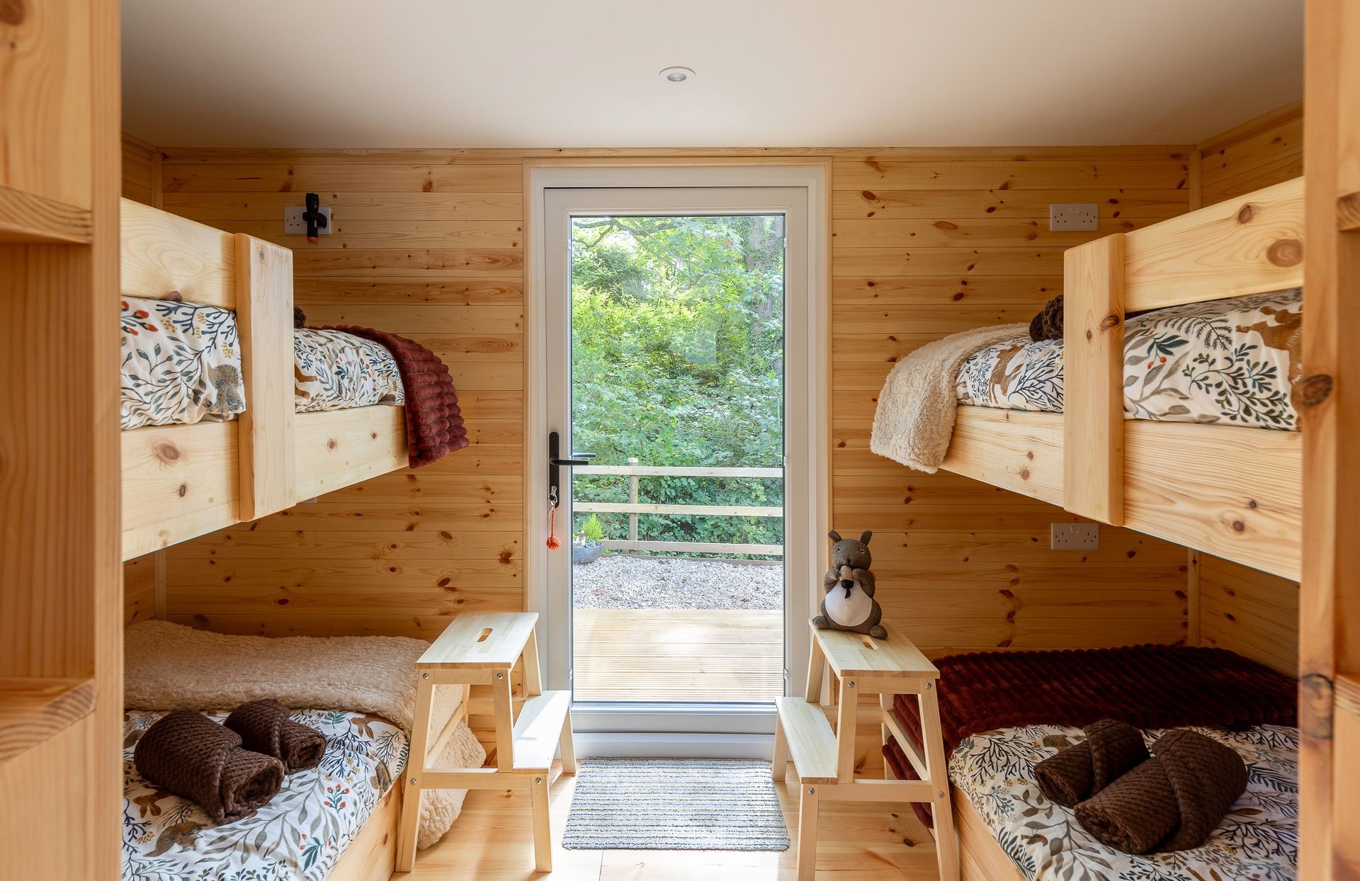 Cabin interior with four bunk beds and a doorway to a small outdoor deck; wooden walls and floors.