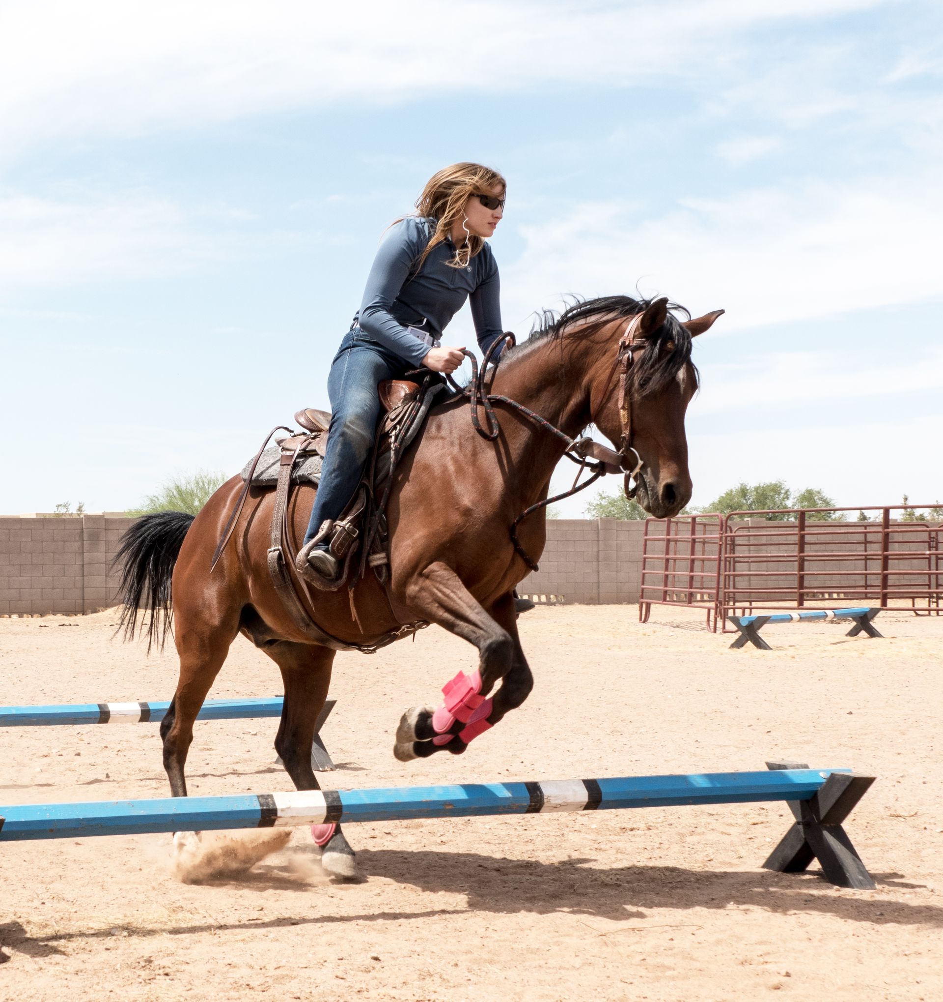 A woman is riding a brown horse over a blue pole