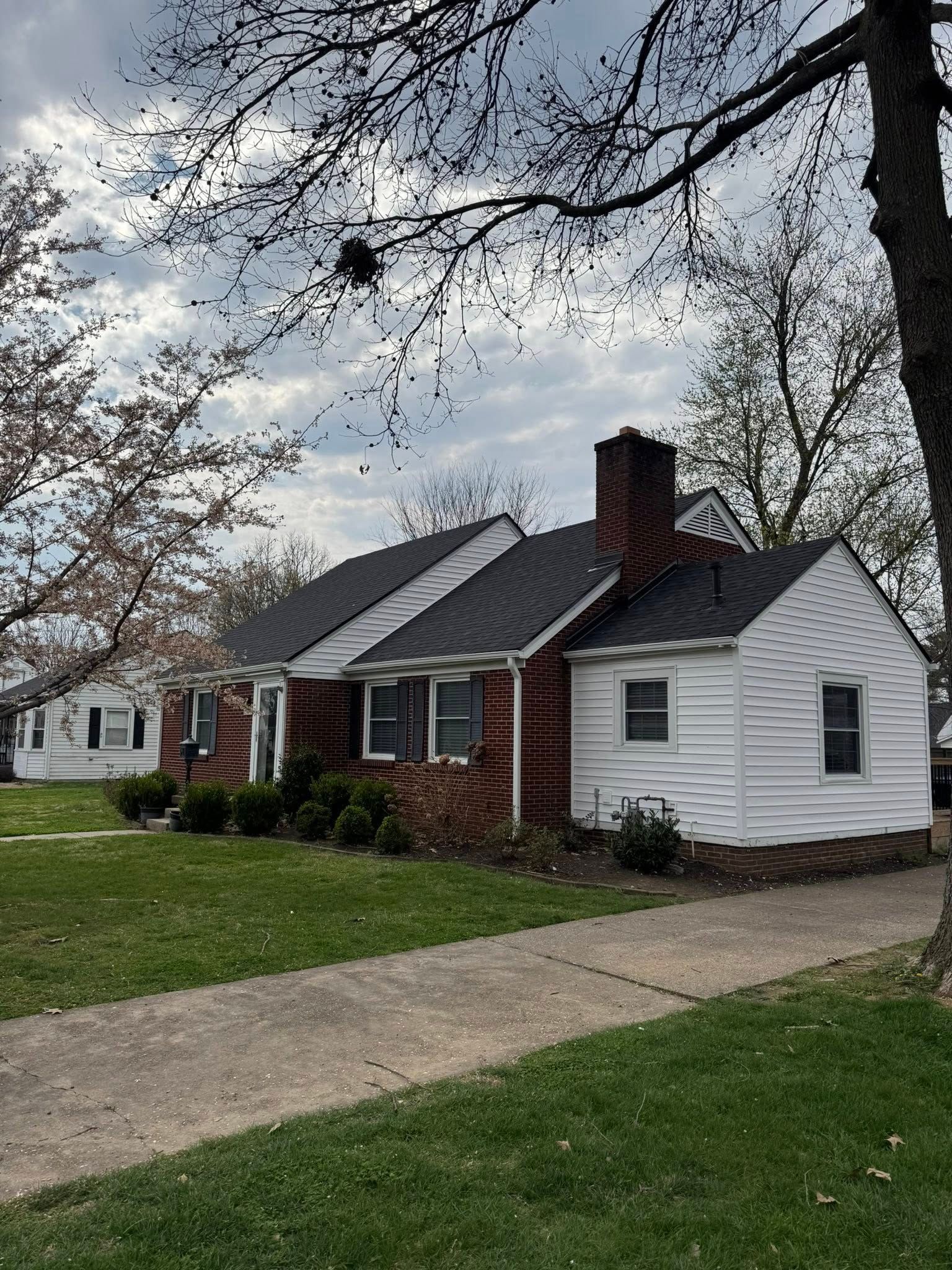 Single-story brick and white house with a front lawn and driveway under overcast skies
