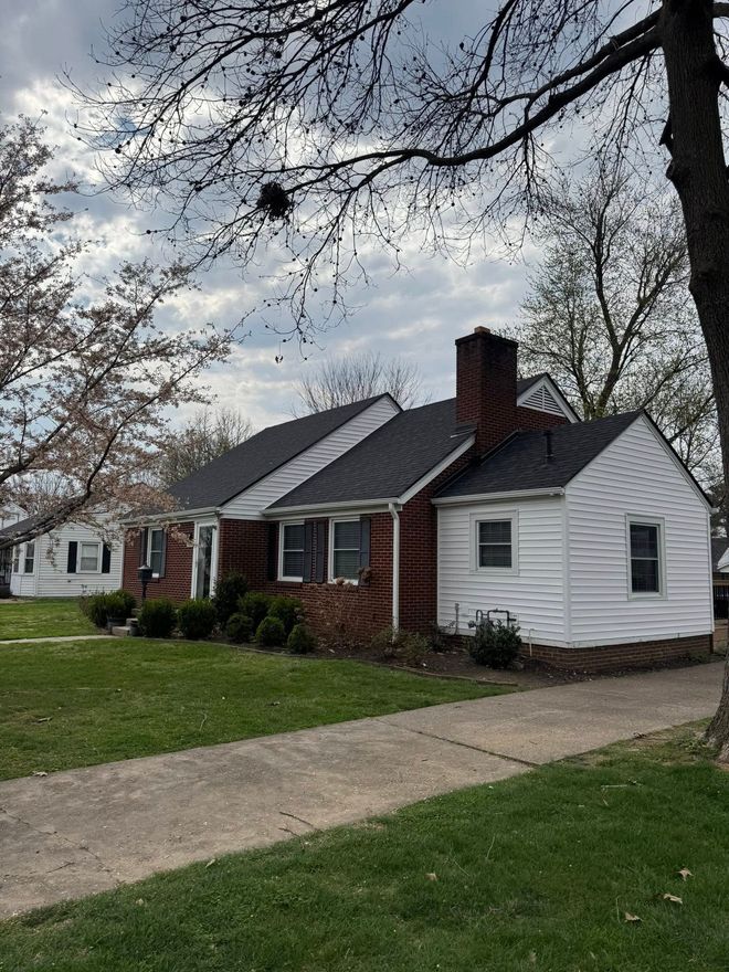 Single-story brick and white house with a front lawn and driveway under overcast skies