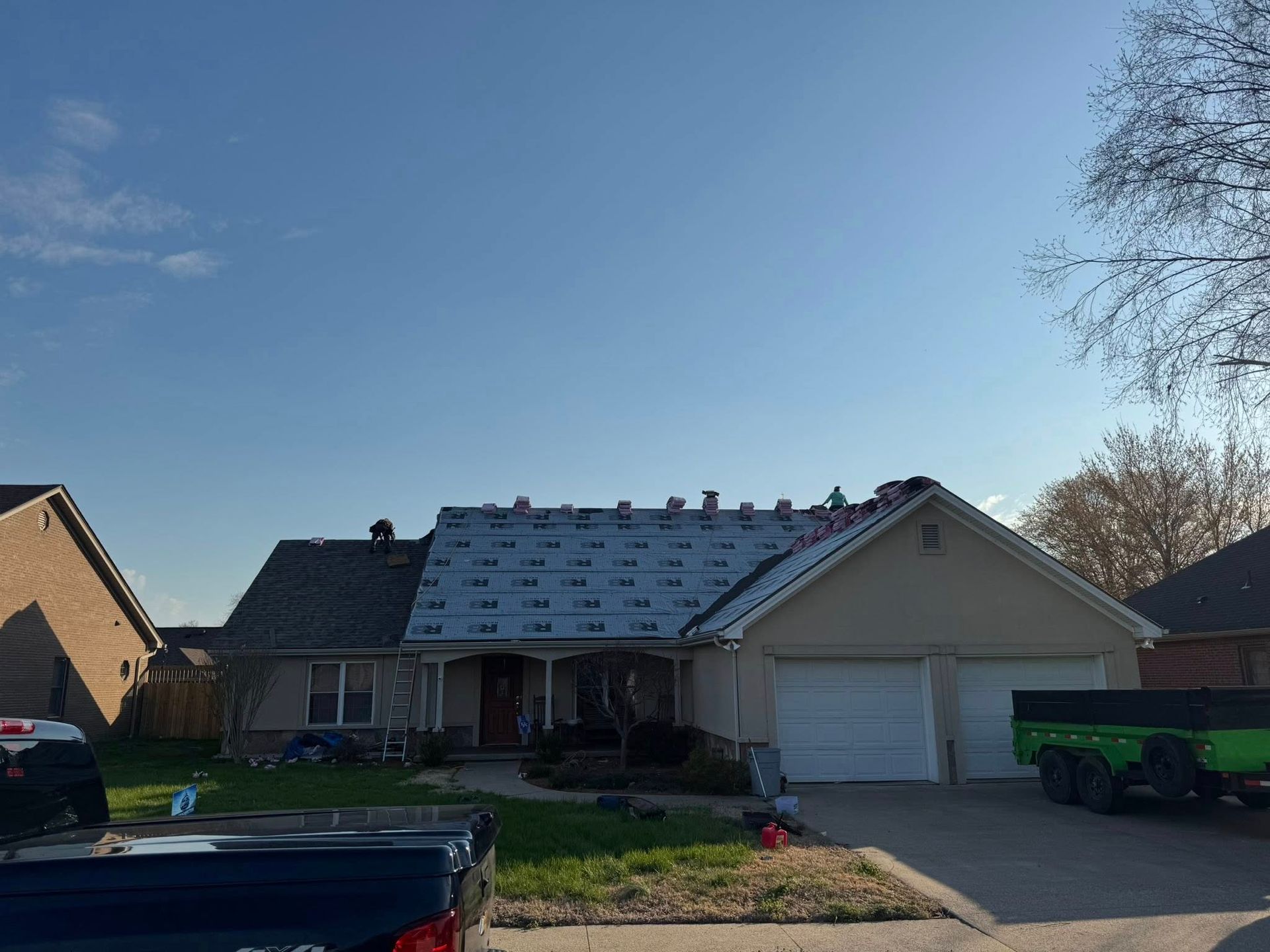 Suburban house with snow-dusted roof, driveway, garage, and parked vehicles under a clear sky