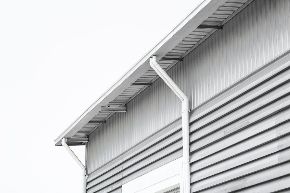 Corner of a gray metal building with a slanted roof and white gutter against a pale sky