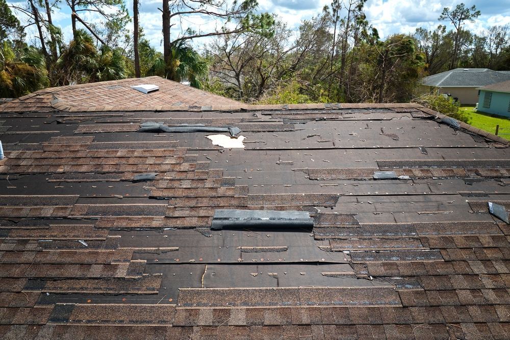 Damaged brown shingle roof with missing patches and visible wear, viewed from above