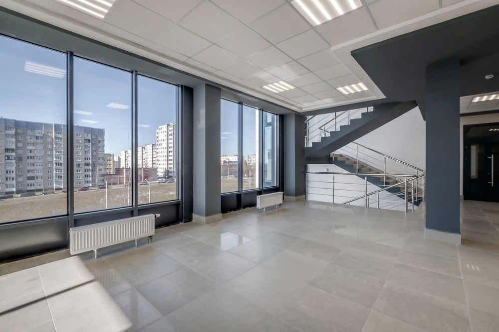 Empty modern office lobby with large windows, gray tile floor, and a stairway