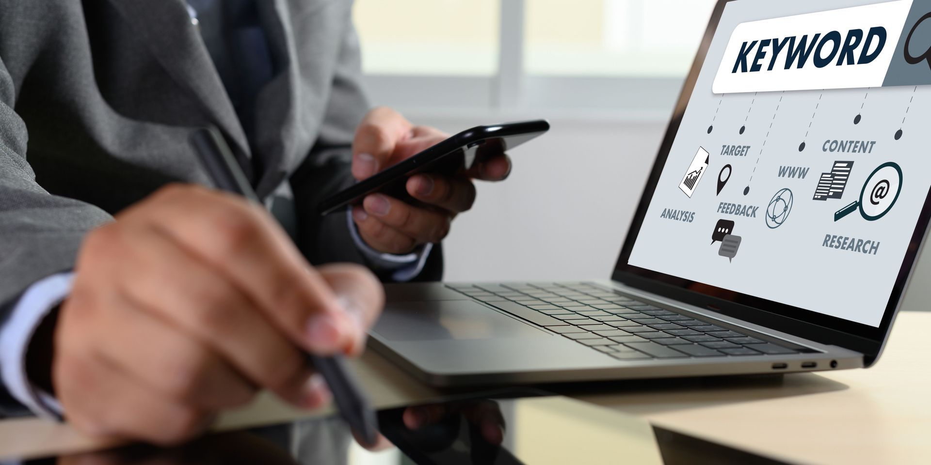 A man is using a laptop computer while holding a cell phone.
