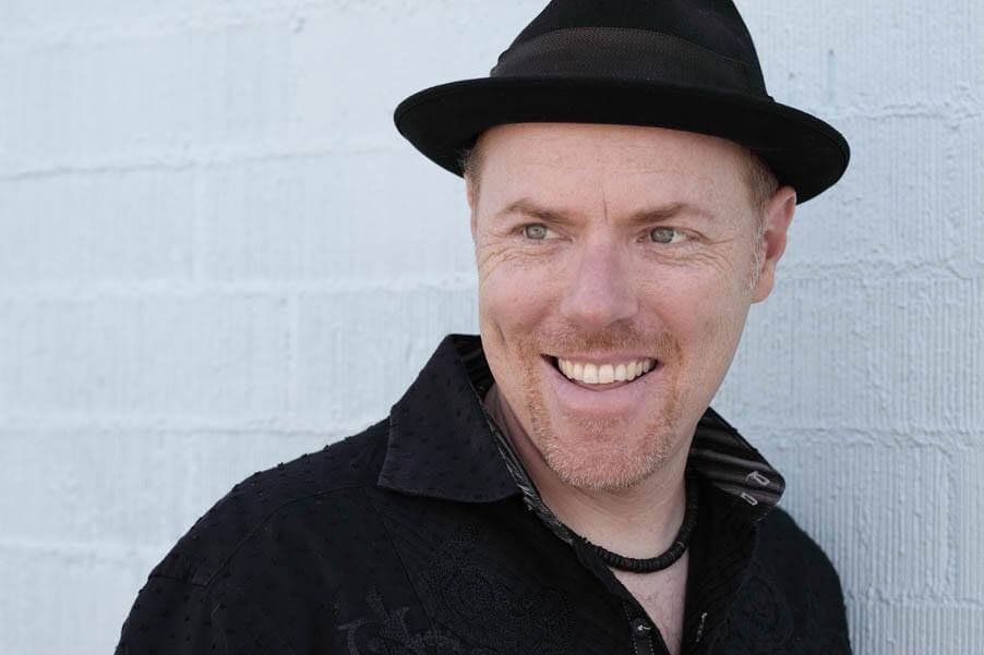 Image may contain man, hat, black shirt, white brick wall