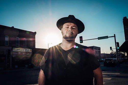 Image may contain black hat, man, sunset, building, street corner, street light