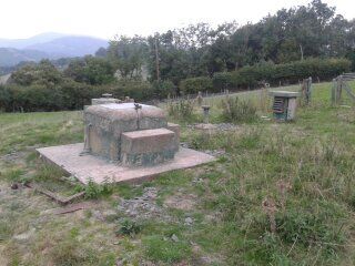 A concrete structure in the middle of a grassy field with trees in the background.