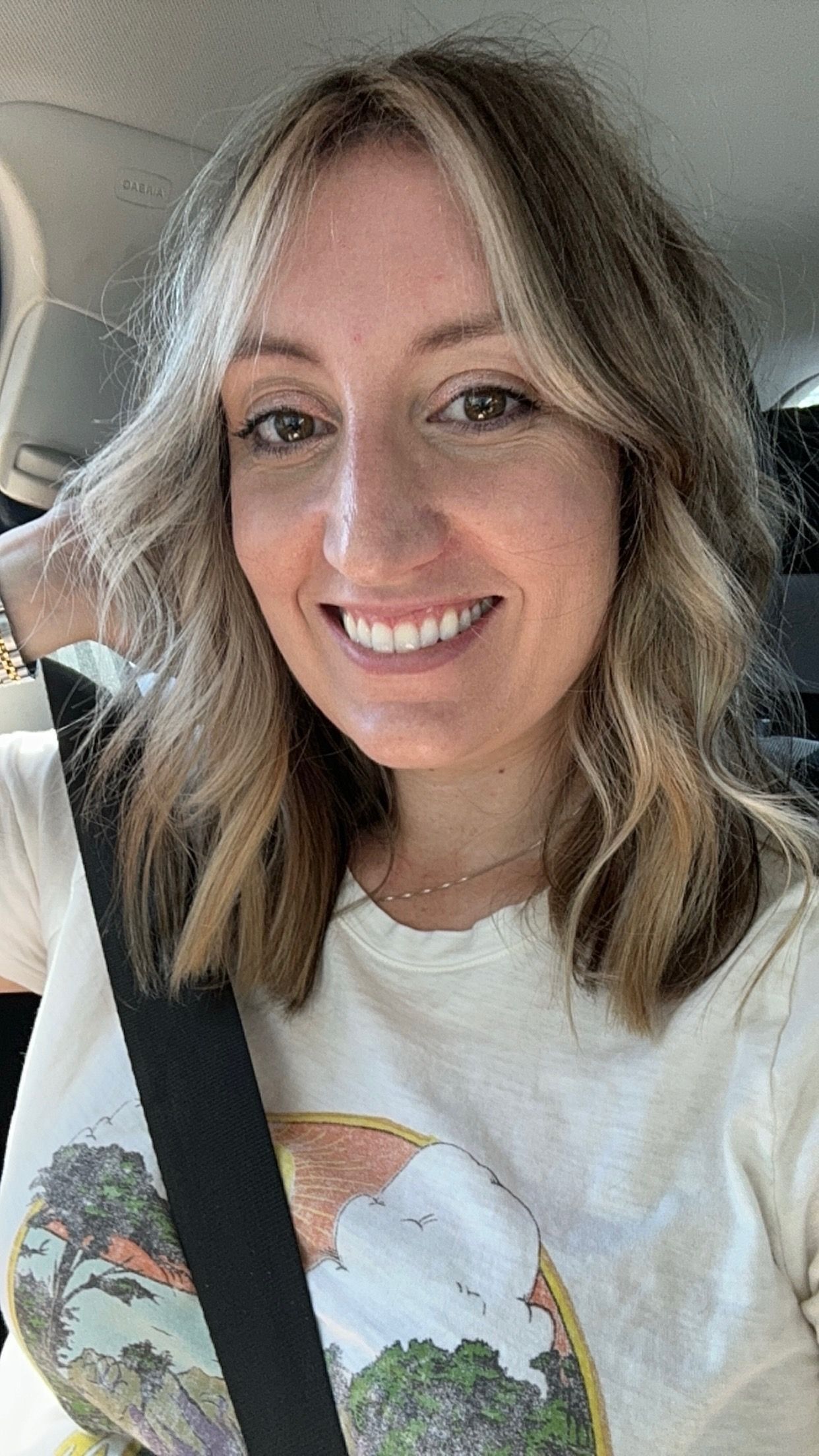 A woman is smiling while wearing a seat belt in a car.
