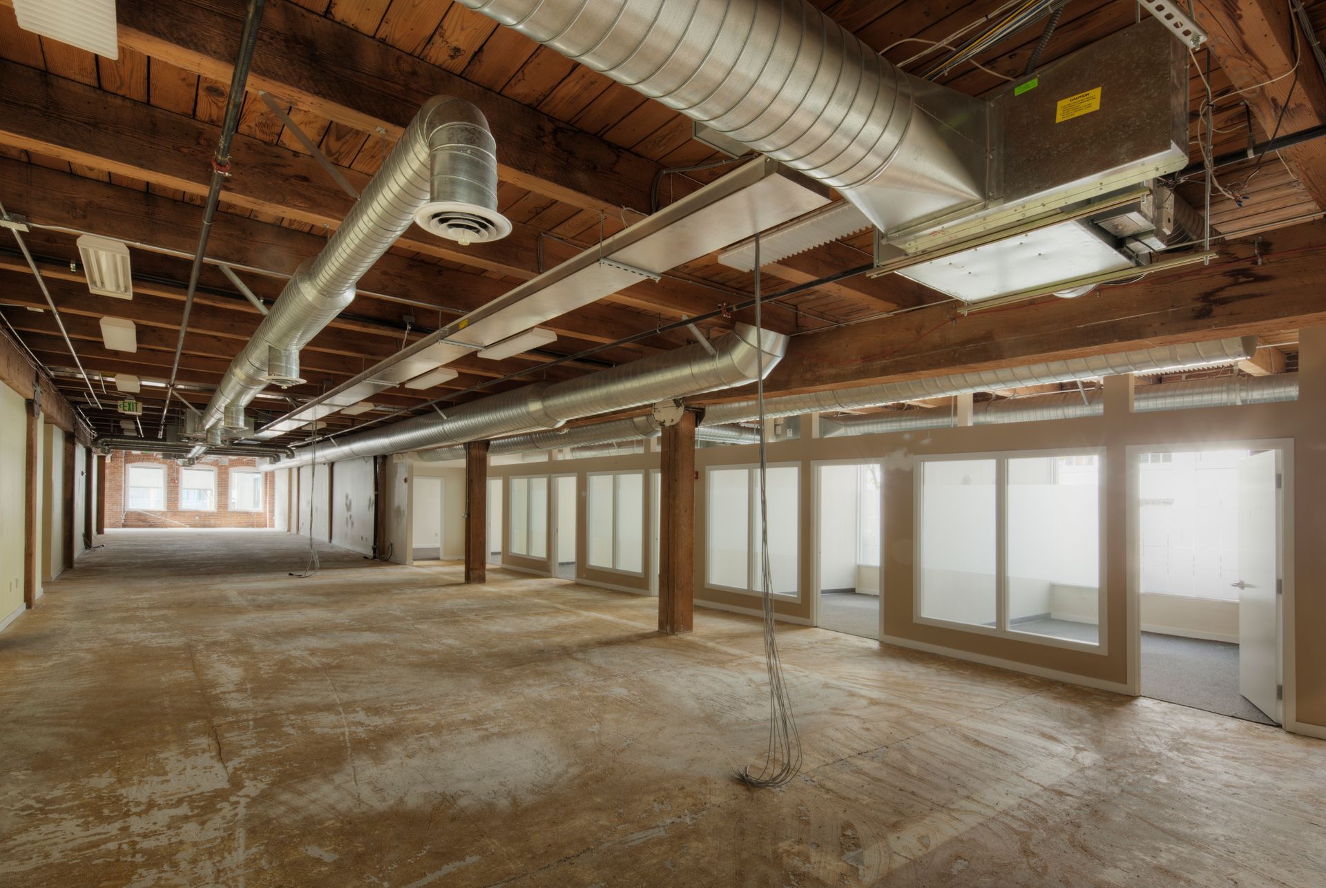 Empty industrial loft interior with exposed ducts, wood beams, and large windows