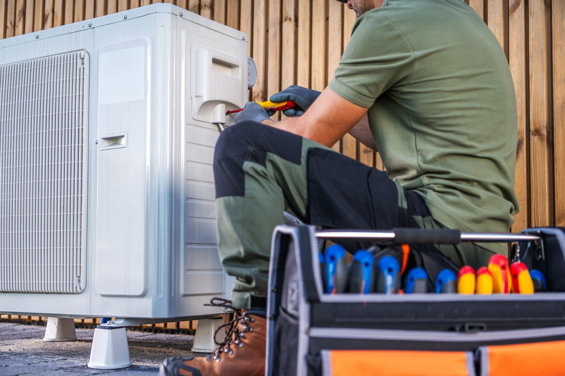 Technician repairing an outdoor air conditioner unit with tools nearby