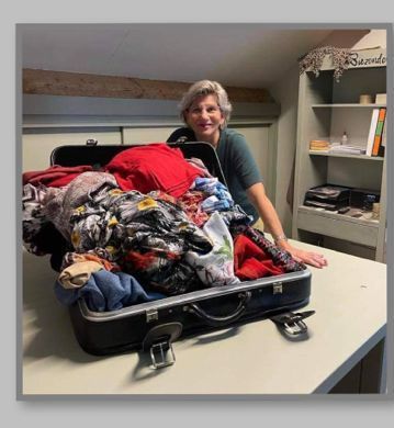 Een vrouw lacht naast een open koffer vol kleren in een kamer.