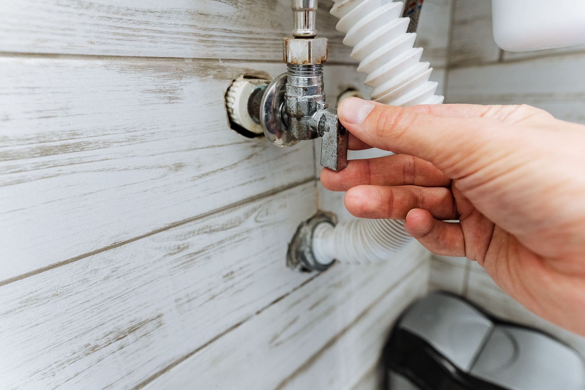 Close-up of a hand adjusting the faucet connection of a toilet.
