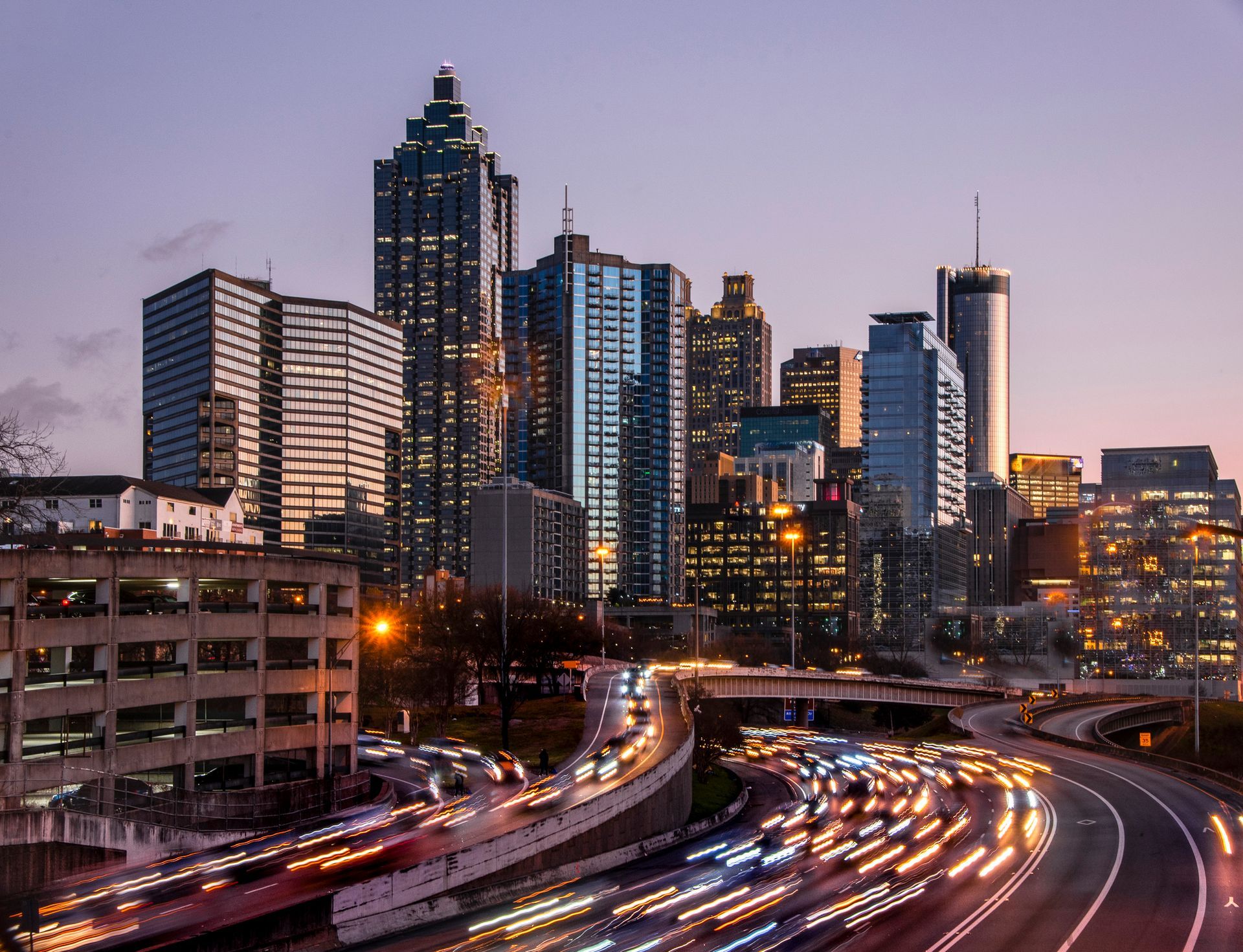 Atlanta skyline with streaks of car lights from highway, under purple-toned sky.