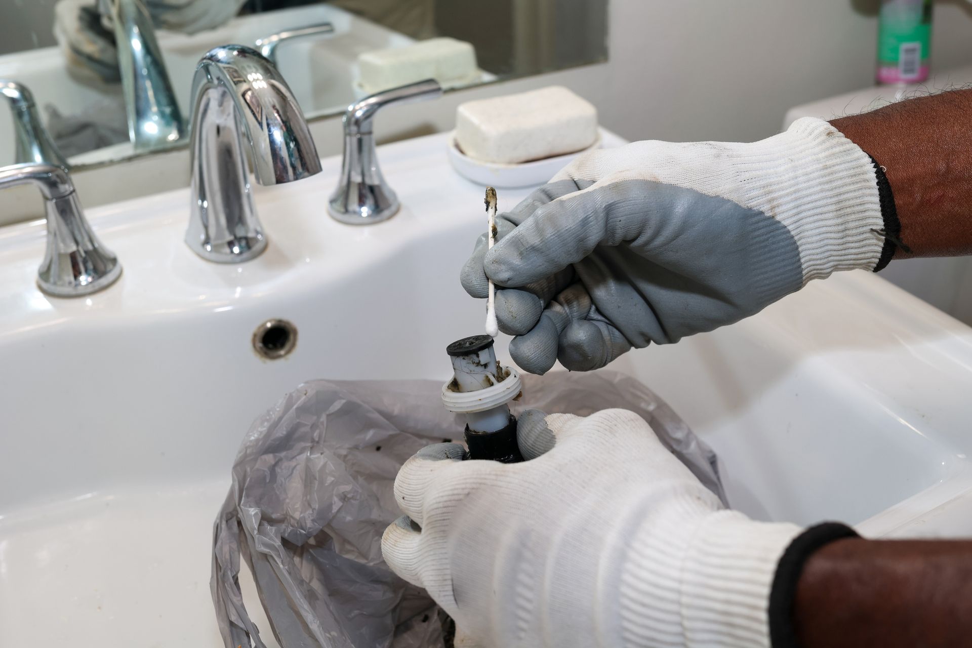 Hands in gloves working on a sink fixture in a bathroom.