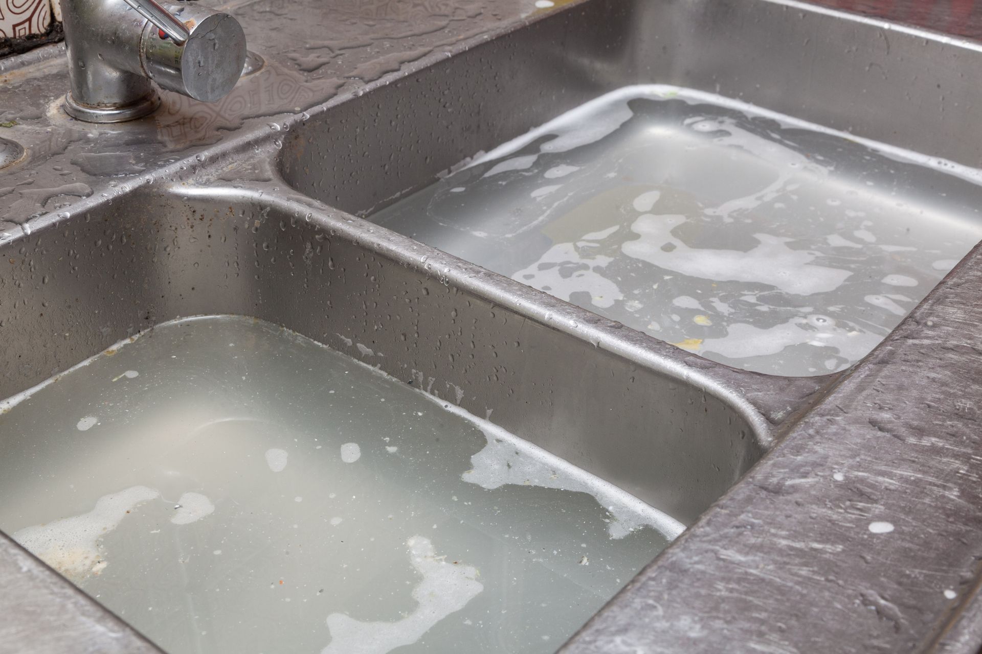 Stainless steel double sink filled with murky water and soap suds.
