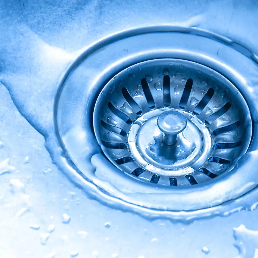 Close-up of a blue-toned stainless steel sink drain with water around it.