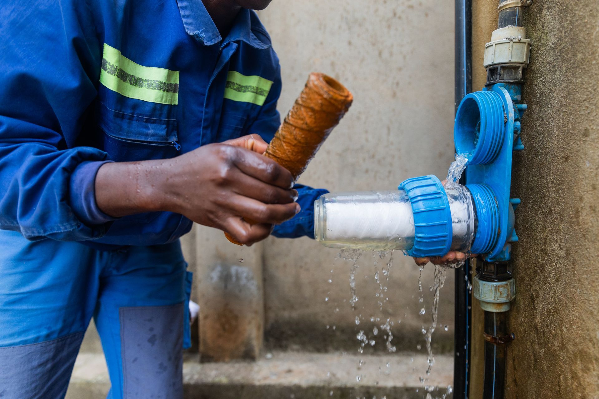 Person replacing a dirty water filter with a clean one connected to a blue water system. Water spills during the process.