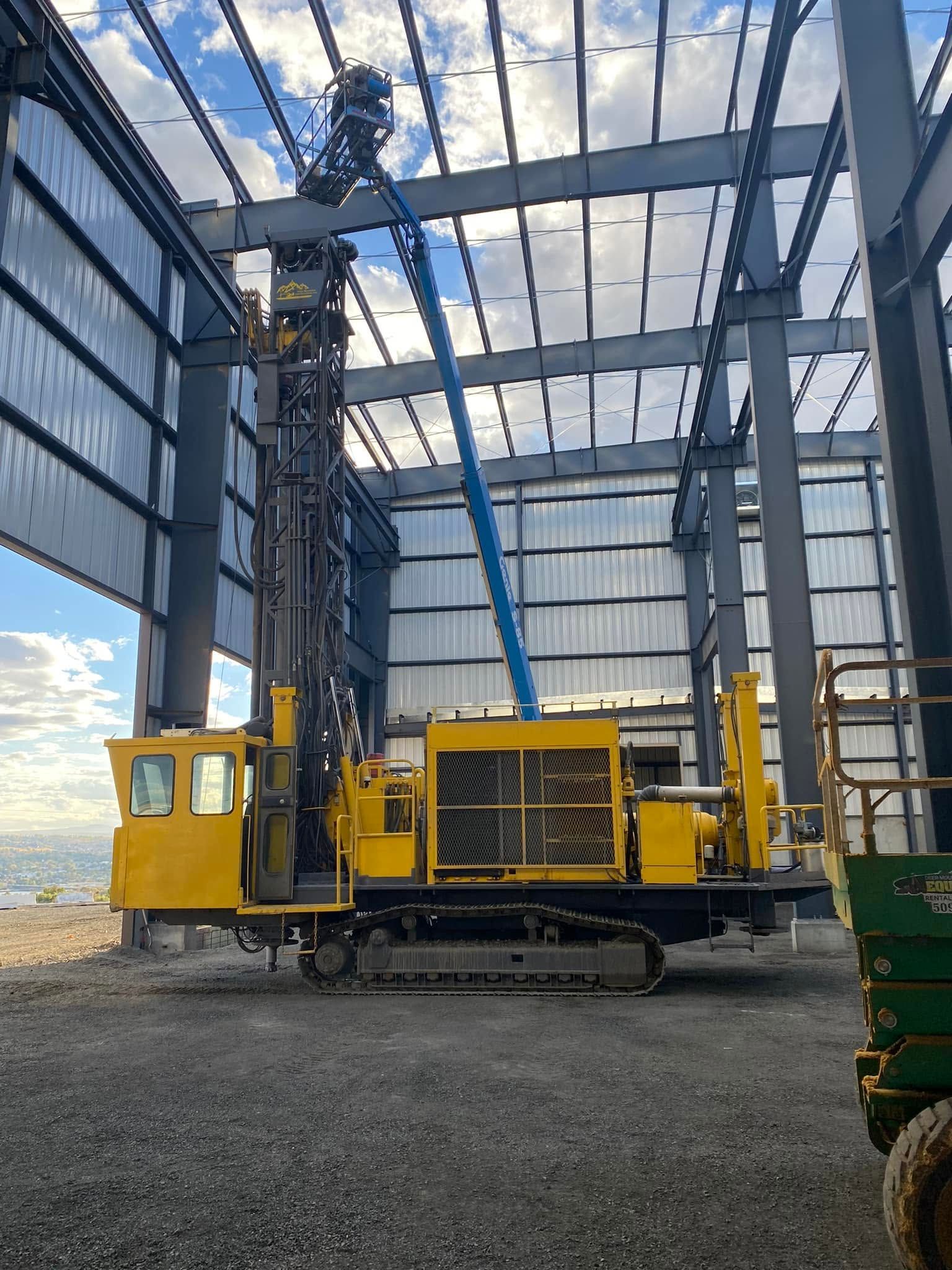 Yellow tracked construction machine inside a steel-frame building under construction.