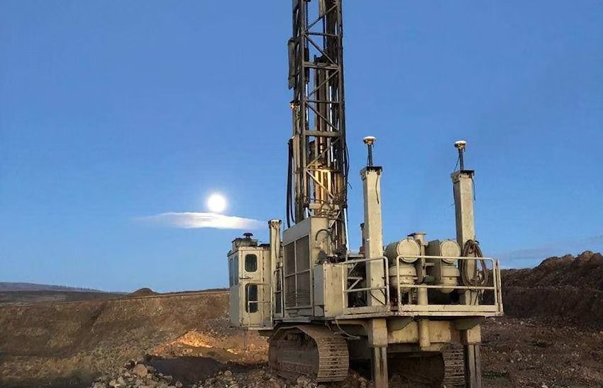 Drilling rig at dusk in a rocky landscape with the moon low in a blue sky