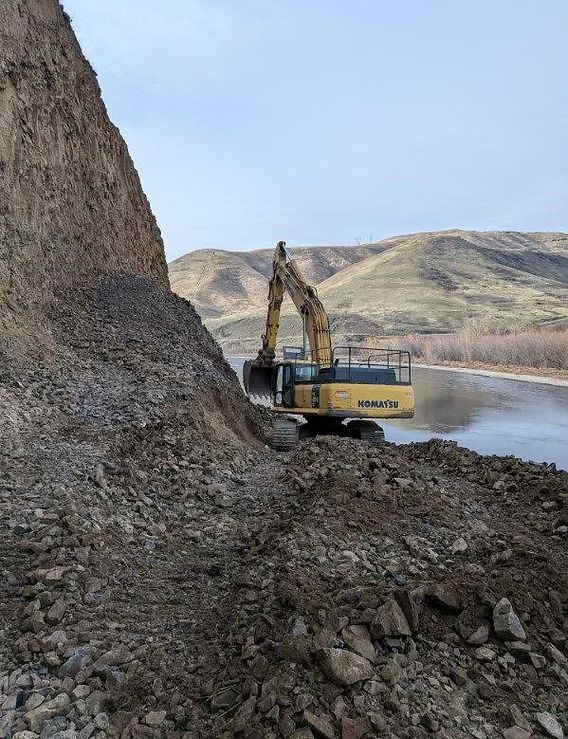 Excavator beside a rocky cliff near a river in a barren landscape