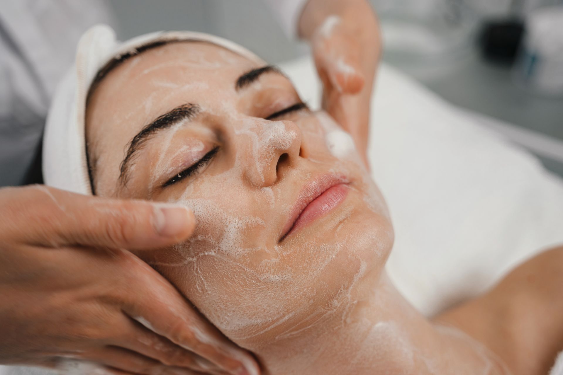 Spa facial treatment with a woman lying down as hands apply a cream facial mask