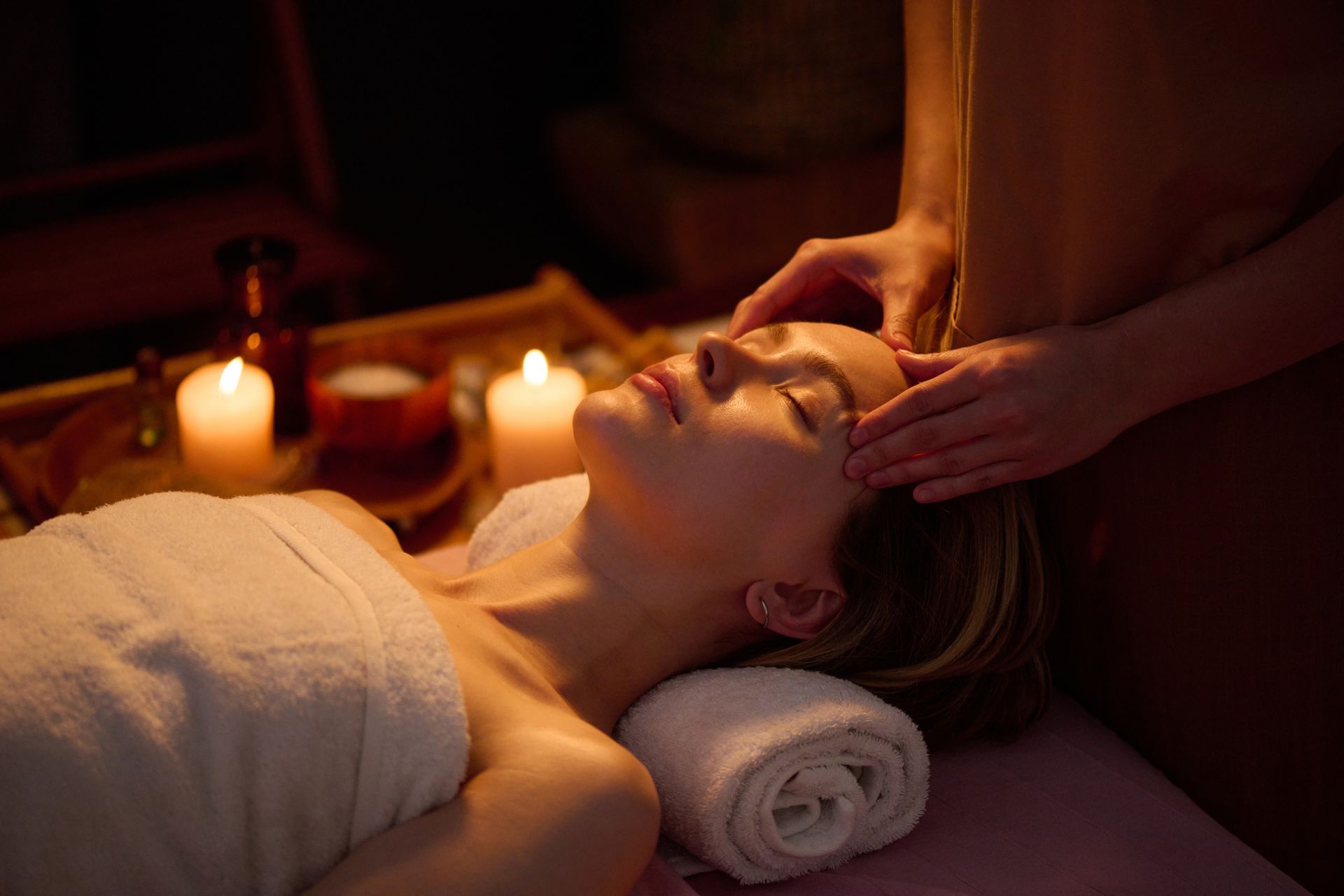 Spa massage with hands pressing oiled back, warm lighting, and a flower near the face