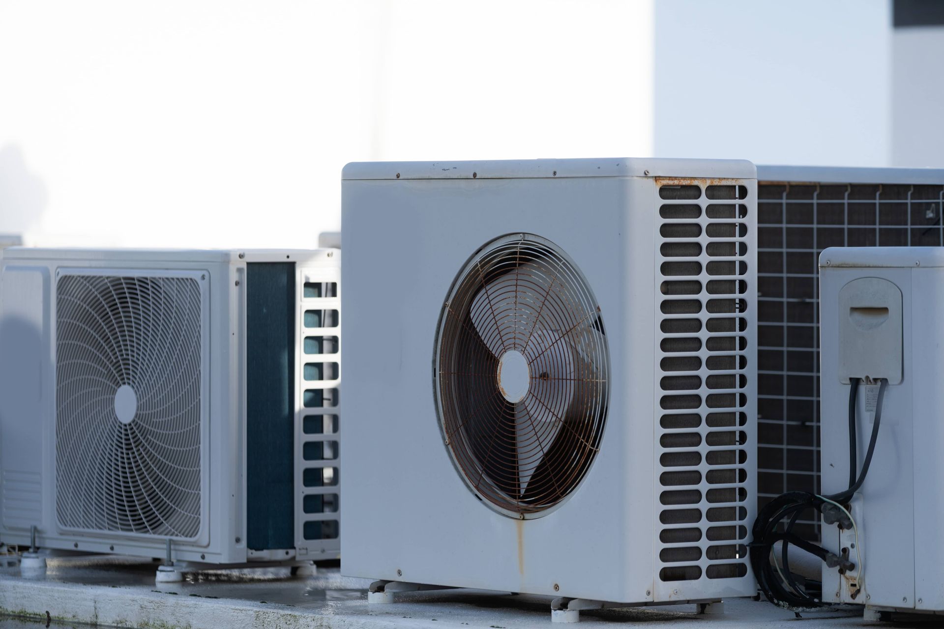 A row of three white outdoor air conditioning units situated on a rooftop against a blurred white background.