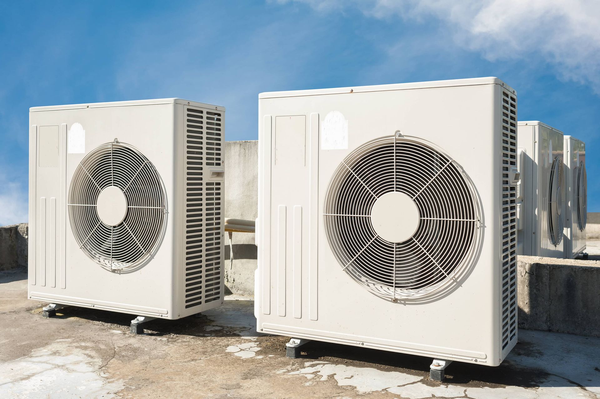 Several light-colored air conditioning condenser units sit on a concrete roof under a blue sky.