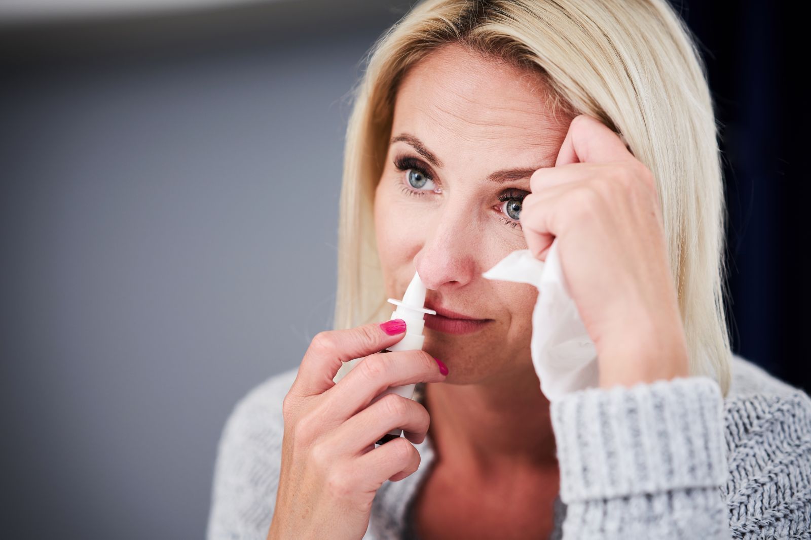 A woman is using a nasal spray to clean her stuffy and blocked nose.