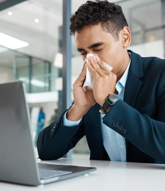 A man in a suit is blowing his nose in front of a laptop.
