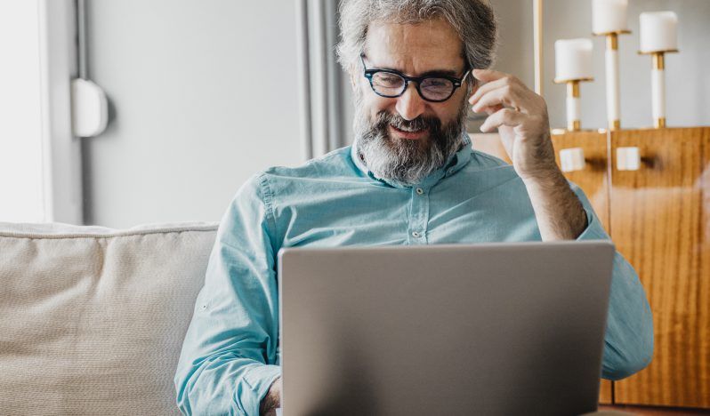 A man is sitting on a couch using a laptop computer.